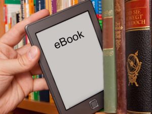 Person accessing an ebook on a tablet and taking the tablet from a stack of books.
