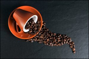A coffee cup on its side spilling whole coffee beans