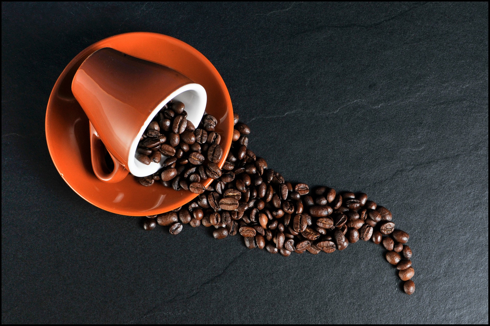 A coffee cup on its side spilling whole coffee beans