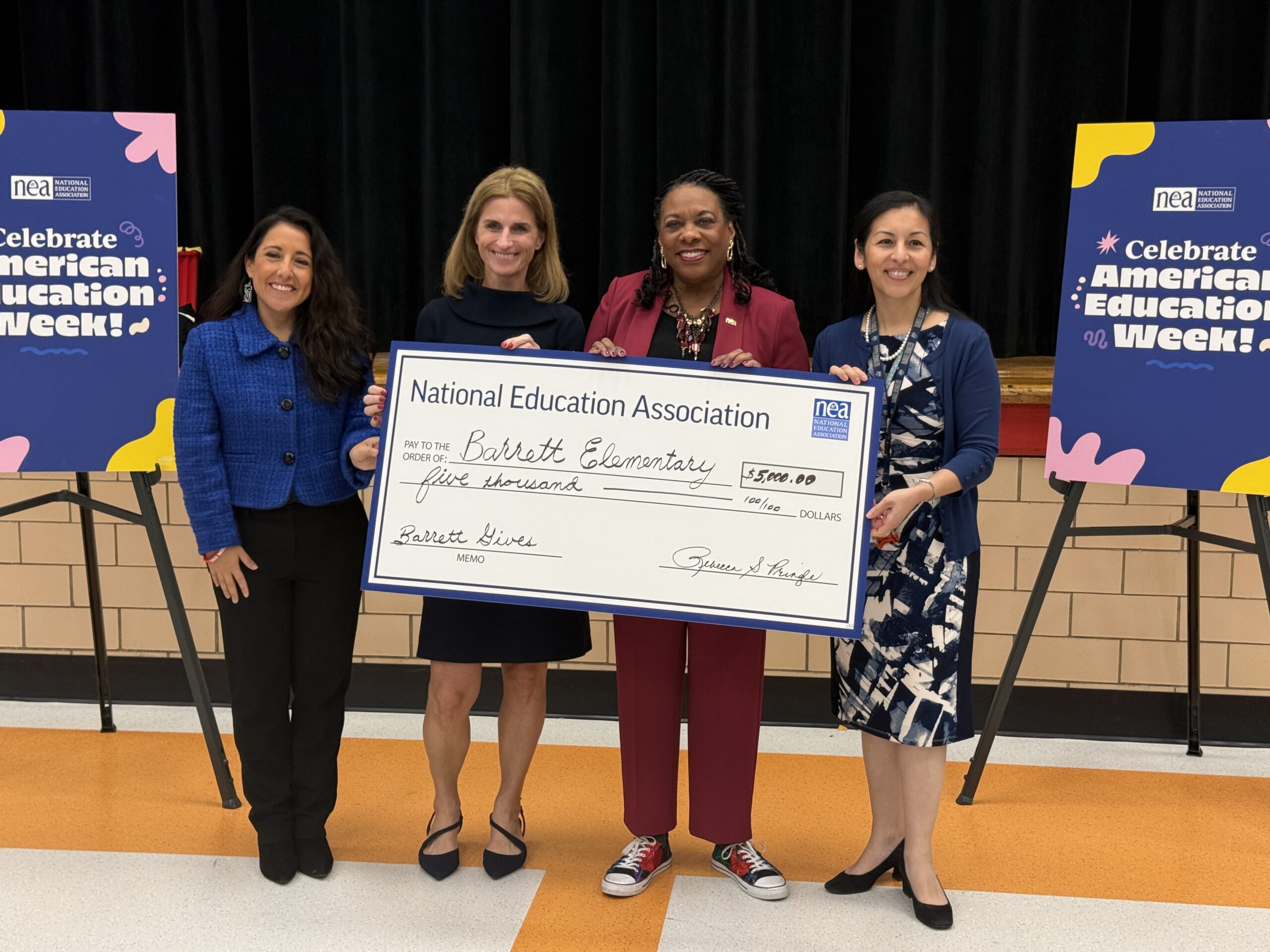 Educators hold huge $5,000 check in the cafeteria