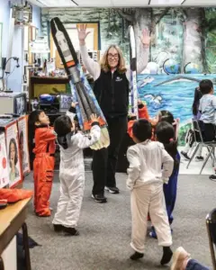 Teacher holds a rocket and PreK Students are dressed as astronauts.